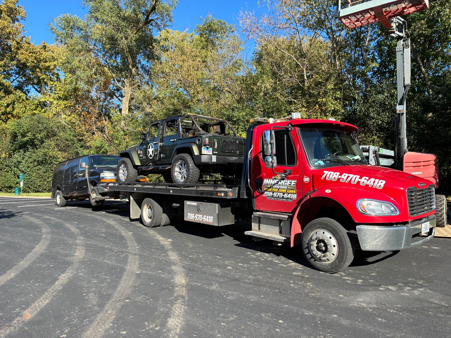 Innergee red flatbed carrying a Jeep Wrangler and towing a van